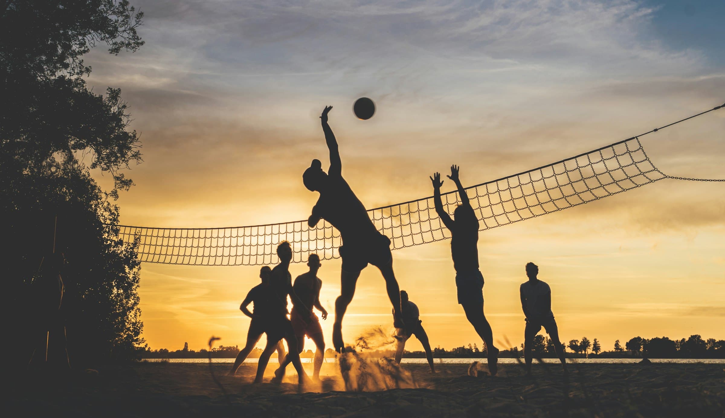 Community members playing beach volleyball together at sunset